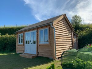 Timber garden office with cedar shingle roof and French doors and windows. It also has a store room to the rear of the building