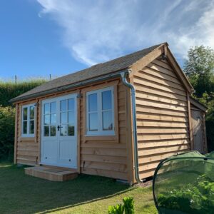 Timber garden office with cedar shingle roof and French doors and windows. It also has a store room to the rear of the building